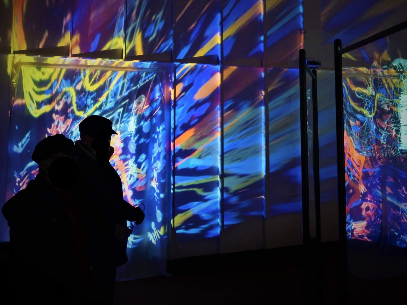 The shadows of two people in front of a very colourful projection